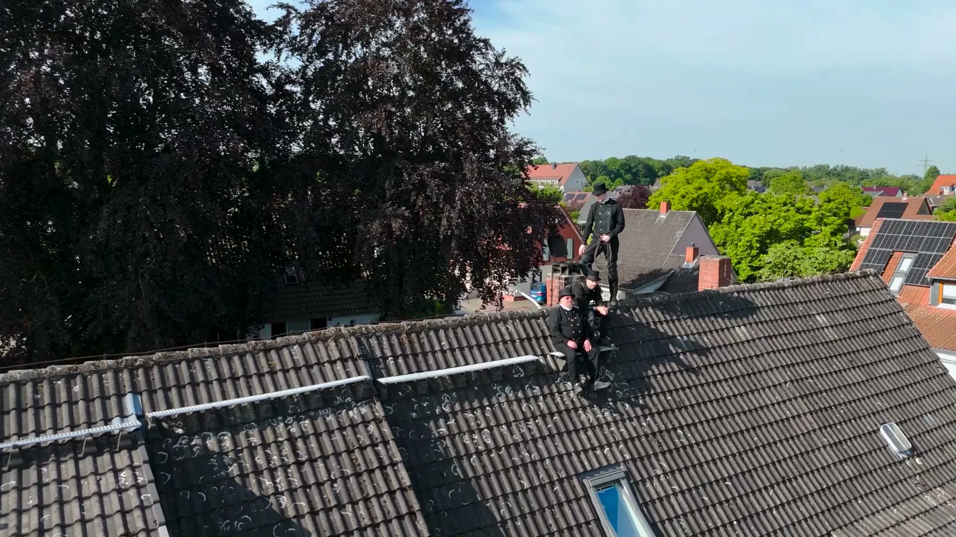 Das Team in Schornsteinfeger-Kluft mit Zylinder auf einem Ziegeldach über den Dächern der Nachbarschaft